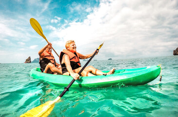 Happy retired couple enjoying travel moment paddling on kayak at Angthong marine park in Ko Samui in Thailand - Active elderly concept around world nature wonders - Bright vivid filtered tone - 568895818