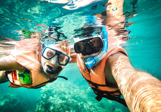 Active senior couple taking under water selfie in tropical sea excursion with water camera - Boat trip snorkeling in exotic scenario - Retired elderly life style concept on scuba diving - Vivid filter