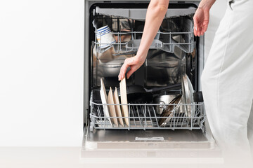 Close-up of female hand putting dirty ceramic dish in the dishwasher. Household and helpful technology concept