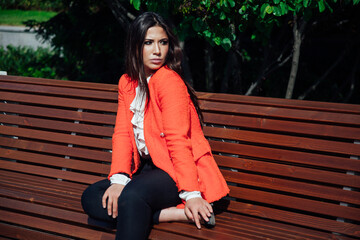 brunette in jacket sits outside on a park bench rest