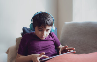 Education concept,High key portrait primary school Kid reading E-book on tablet for homework,Child wearing headphone playing game online on internet,boy sitting on sofa watching cartoon on digital pad
