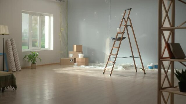 Interior of an empty apartment during renovation. A stepladder, stacks of cardboard boxes on the floor, rolls of wallpaper, paint buckets and a green flower in a brightly lit room.