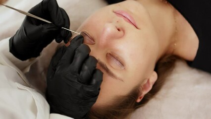 Beautician separates eyelashes with using a special tool with a needle and bends into silicone curlers. Preparation for lamination of eyelashes in a beauty salon.	