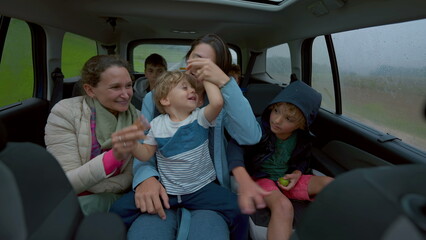 Fototapeta na wymiar Happy people inside car backseat waving hands laughing and smiling together. Family traveling in vehicle interior on road