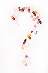 Pills are laid out in the form of a question mark, on a white background. Top view.