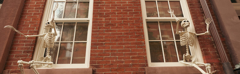low angle view of creepy Halloween skeletons on white windows of brick house in New York city,...