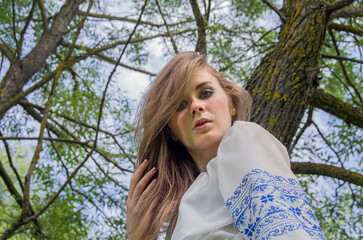 Naklejka premium A girl in a long blue skirt and an embroidered shirt among the green meadow and marsh grass and willow trees.