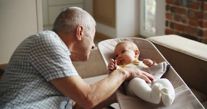 Grandfather Holding Newborn Baby Granddaughter by the hand and talking to her at home. High quality 4k footage
