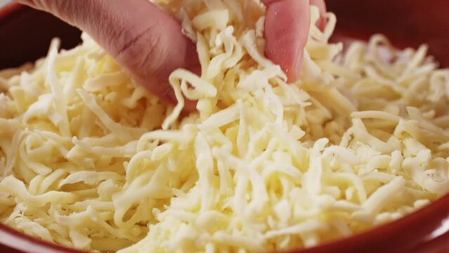 Grated pizza cheese mozarella close up, chef hand touching cheese for Italian pasta or pizza. Macro close up of cheddar cheese.