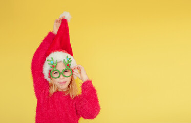 Funny Laughing Christmas girl with red fluffy Santa Hat on yellow background. Copy space