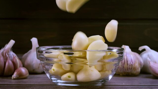Fresh garlic clove peeled falling in glass bowl. The raw garlic is one of the most popular ingredients of the basic recipes with nutritional properties, infamous aroma and health benefits. Slow motion