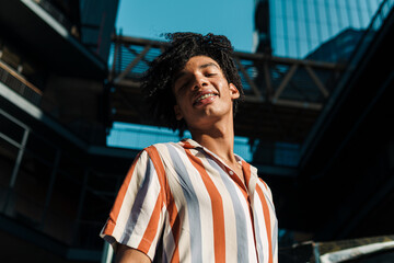 joven latino con afro y frenillos, sonriendo en la ciudad. de pie en la ciudad.
