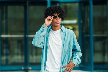 modelo hombre de color posando con anteojos y ropa urbana en la ciudad