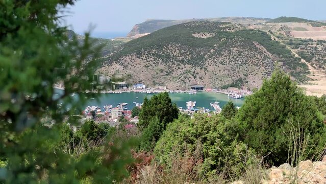 Cityscape of Balaklava city (part of Sevastopol) on the coast of Black sea in a sunny summer day. Clear blue sky. Selective focus. Blurred green juniper tree branch in the foreground. Travel theme.