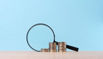 A stack of metal coins and a plastic magnifier on a blue background. The concept of increasing...
