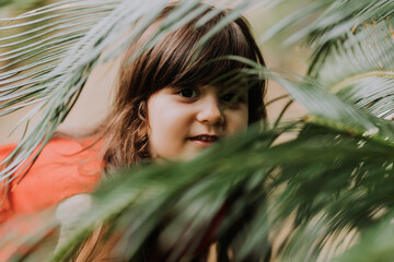 Naklejka premium cute brunette girl in a red dress walks in summer among palm trees in the park