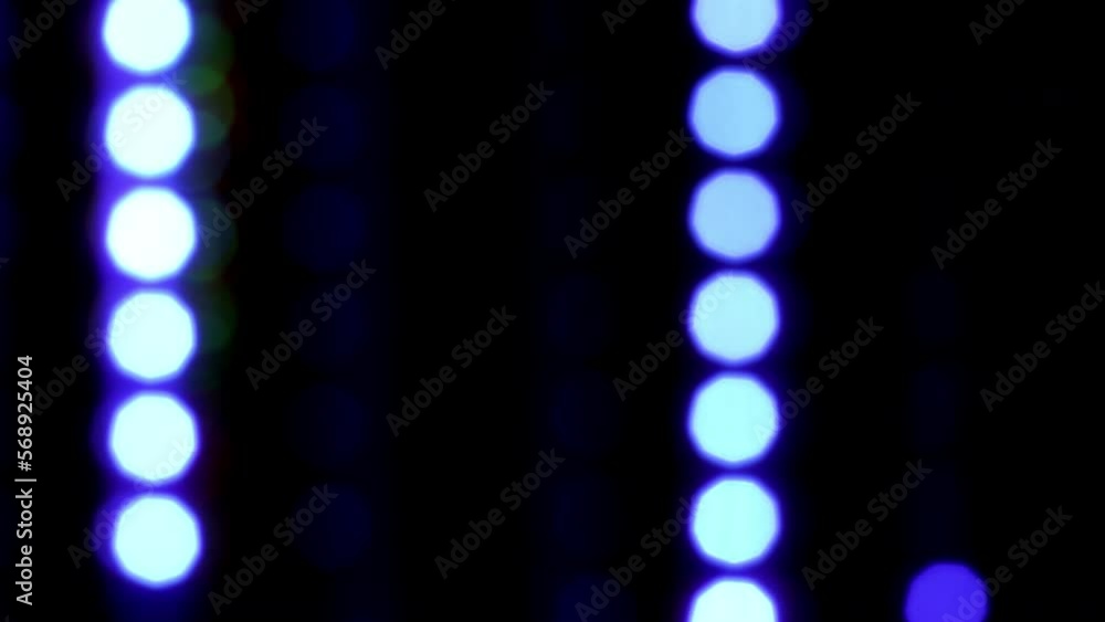 Wall mural vertically falling blue blurry dots. blue bokeh with reflexes fall down on a black background. defoc
