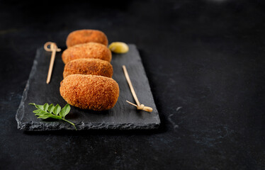 Serving of gourmet style ham croquettes with a black background.