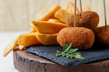 Close up view of snack of ham croquettes and chips on a wood.