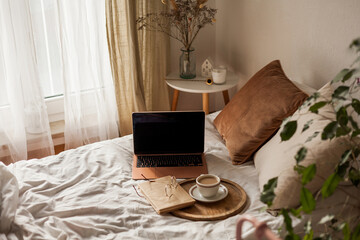 Cup of hot cappuccino, a book, glasses, a laptop on the bed. Work online at home. Home Office. Internet.