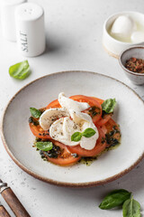 Caprese salad in modern feed with tomatoes, basil, mozzarella, pesto. Traditional Italian food with cutlery on white background, menu