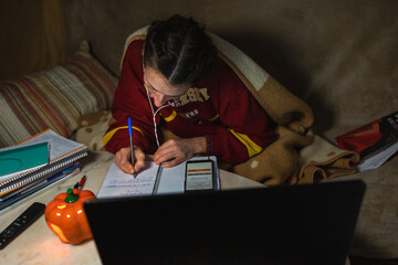 A girl in a cozy home environment does homework, concentrates on writing something in a notebook.