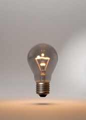 Classical style lightbulb E27. Hovering over studio floor. Burning softly. Idea metaphor. Glowing thread. Bright room.