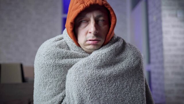 man is freezing wrapped in a blanket because of the weak heating in the apartment