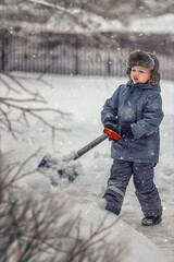 Baby boy in a fur hat digs snow with a shovel in winter