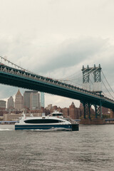 modern yacht on Hudson river under Manhattan bridge and cloudy sky in New York City.