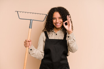 Young african american gardener woman holding a rake isolated cheerful and confident showing ok...