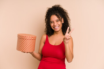 Young african american woman holding a valentines day box gift isolated joyful and carefree showing a peace symbol with fingers.