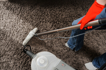 Housekeeper is extracting dirt from carpet using dry cleaning extractor mop machine. Cleaner girl...