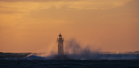 stormy weather, the rough sea are clashing into the lighthouse, during the sunset 
