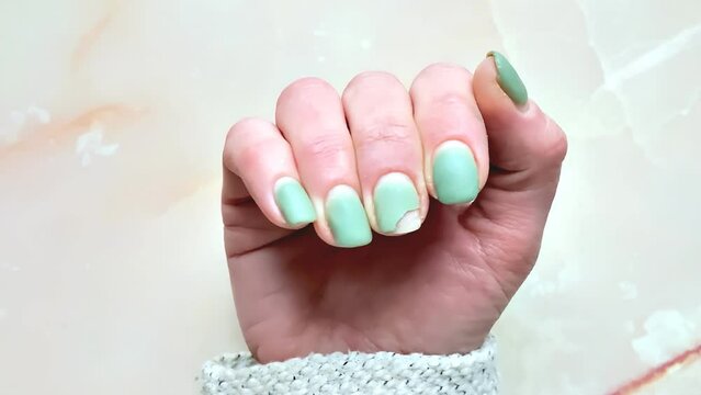 Close-up damage female green shellac or gel polish on the nails, Home manicure concept. Fashion beauty,Glitter nail womens polish scratches on marble background with copy space,video footage.