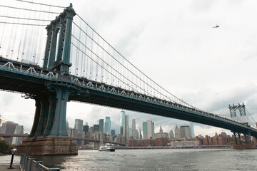 Obraz premium scenic view of Manhattan bridge and modern skyscrapers under cloudy sky in New York City.