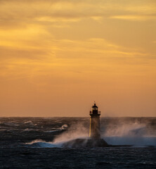 sunset over the sea, in the foreground a lighthouse, where the big waves a crashing into the solid build of the lighthouse 