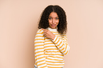 Obraz premium Young african american curly woman isolated smiling and pointing aside, showing something at blank space.