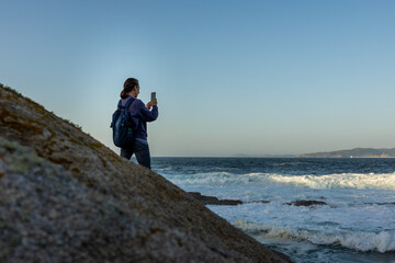 Obraz premium A girl stands on a rock and takes a photo of the ocean