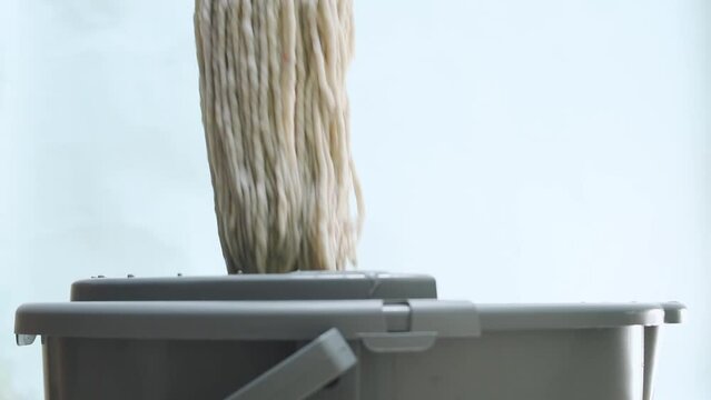 Man squeezing a mop on a plastic mop squeezer on blue background