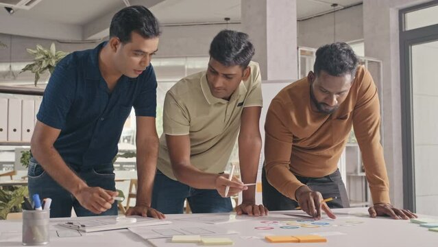 Team of Indian mobile app developers working with paper sketches while discussing layout design in office