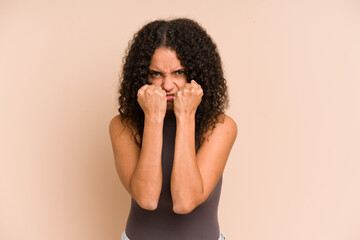 Young african american curly woman isolated throwing a punch, anger, fighting due to an argument,...