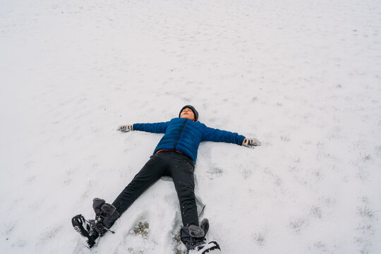 A child laying in the snow making snow angels. 