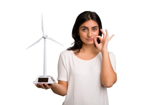 Young Indian woman holding a small wind energy mill isolated with fingers on lips keeping a secret.