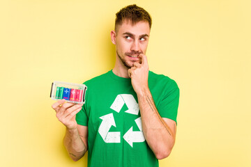 Young man holding batteries to recycle them cut out isolated relaxed thinking about something looking at a copy space.