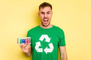 Young man holding batteries to recycle them cut out isolated screaming very angry and aggressive.