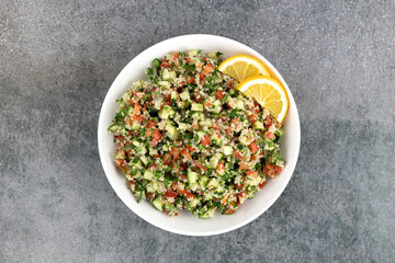 Obraz na płótnie Canvas Tabbouleh salad with quinoa, tomatoes, cucumbers, parsley, mint and lemon juice on a gray background. Top view. Healthy vegetarian salad.