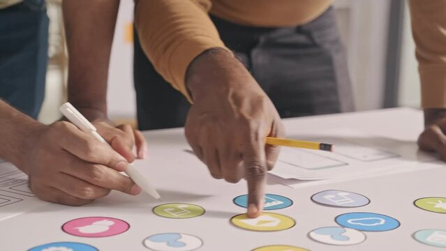 Close up shot of male UX designers discussing icons and taking notes of wireframe sketches at office table while developing mobile app interface