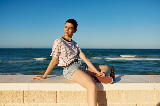 Young woman with beer sitting on border near sea
