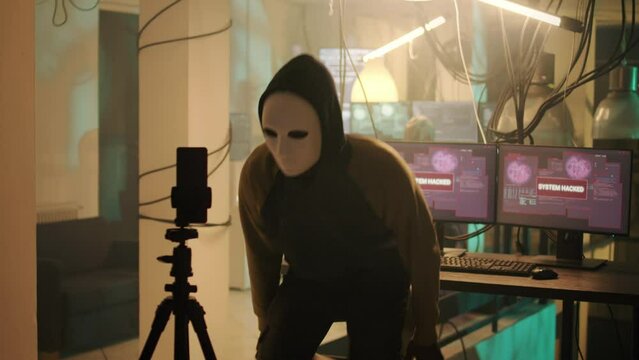 Male spy with anonoymous mask filming live threat video, asking for ransomware instead of leaking important data. Young person threatening to expose information, online cybercrime.